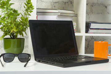 Laptop, glasses, orange mug with coffee and green flower