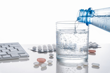 Gesundheit, Medizin, Tabletten, Wasserglas und Tastatur spiegelnd auf heller Tischplatte