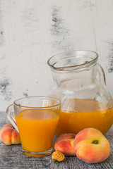  Freshly prepared natural peach juice with pulp in a glass jug and in a mug, next to ripe peaches on a dark wooden table. The concept of healthy eating.