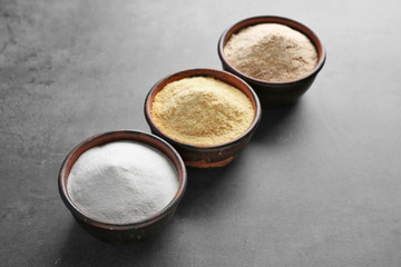 Wooden bowls with different types of flour on gray background