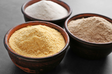 Wooden bowls with different types of flour on gray background