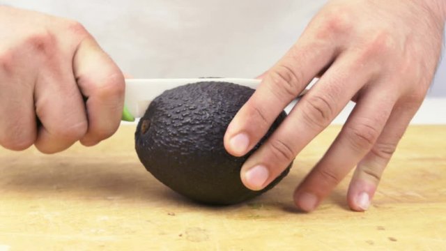 Close Up Of Hands Slicing Avocado In Half With Ceramic Knife On Wooden Board