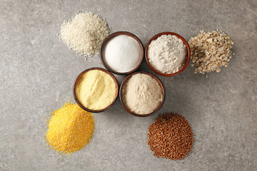Bowls with different types of flour on gray background