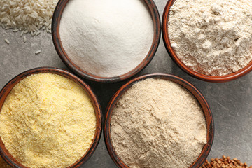 Bowls with different types of flour on gray background