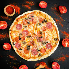 Italian delicious pizza with ingredients and spices on dark background. Flat lay, top view.