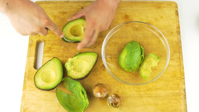 Peeling Avocados With A Spoon Into Glass Bowl On Wooden Table Top View