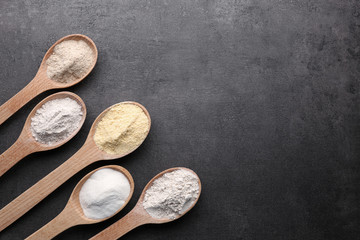 Wooden spoons with different types of flour on gray background