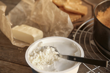 Spoon in bowl with cream cheese for cake on wooden table