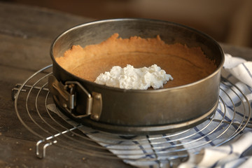 Baking pan with dough and cheese for cake on kitchen table