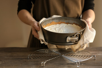 Woman holding baking pan with raw cheese cake in kitchen