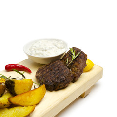Close-up of grilled beef medallion served with roasted potato on the white background