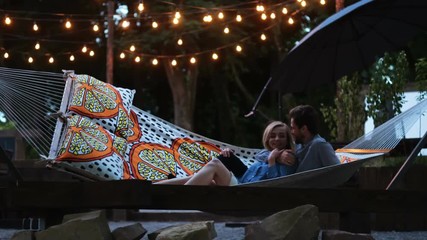 Loving couple swinging in hammock on the background of evening park lanterns