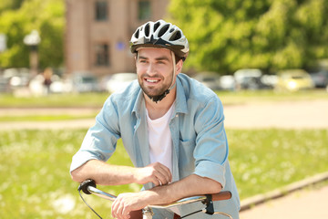 Handsome young man with bicycle and helmet in park on sunny day