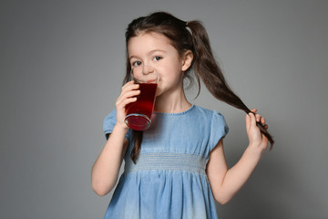Cute little girl drinking juice on grey background © Africa Studio
