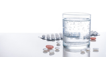 Gesundheit, Medizin, Tabletten, Wasserglas spiegelnd auf heller Tischplatte, Hintergrund