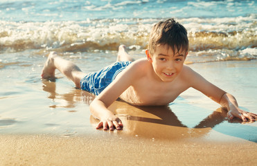 Child lying on the beach with swimming mask and flippers. Boy on vacation at sea