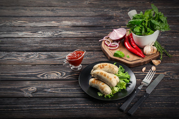 Black plate with delicious grilled sausages on wooden dark table