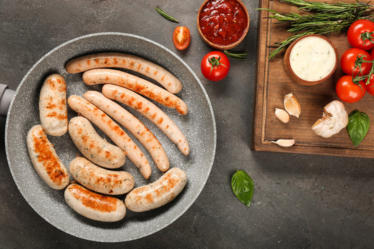 Grey frying pan with delicious grilled sausages on kitchen table, top view