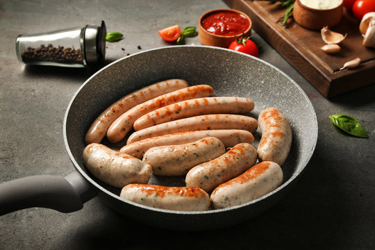 Grey frying pan with delicious grilled sausages on kitchen table