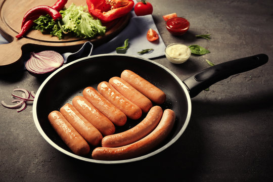 Black frying pan with delicious grilled sausages on kitchen table