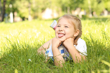 Naklejka na ściany i meble Cute little girl lying on green grass in park