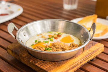 Breakfast at Cafe, The plate with eggs, meat topped green onion and toasts. Wooden table, closeup