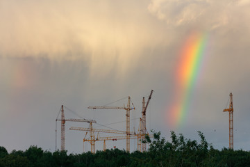 Construction cranes. Rainbow in the sky. Thunderclouds. Evening.