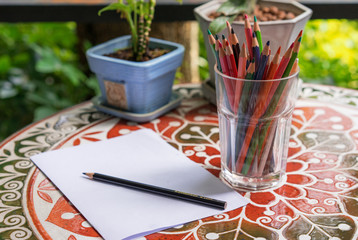Color pencils in glass and white paper on a table
