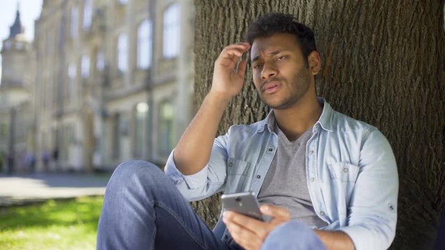 College student reading newsfeed on phone, getting disappointed with news, upset