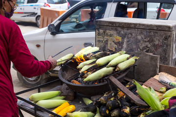 A woman is cooking corn on the coals on a street of dusty Kathmandu, Nepal. 