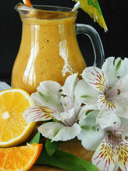 Yellow smoothie made of peach, citrus, lemon and mint surrounded by fruit, flowers and decorated with a little umbrella
