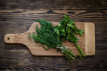 Parsley and dill on a cutting board, wooden background