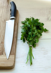 Fresh organic parsley with knife on wooden cutting board.