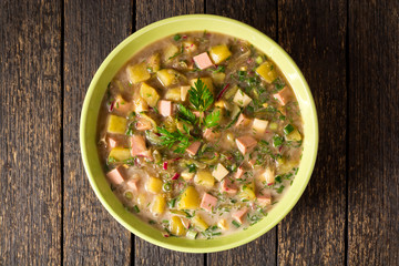 Okroshka. Traditional Russian summer cold soup with sausage, vegetables and kvass in bowl on wooden background.
