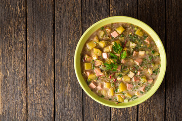 Okroshka. Traditional Russian summer cold soup with sausage, vegetables and kvass in bowl on wooden background.