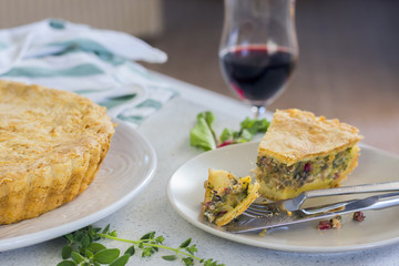 Traditional French pie- quiche  with chard on a light plate and a glass of red wine in the background. Selective focus.