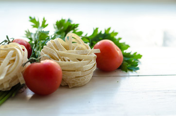 Tagliatelle with ingredients for cooking pasta. Curly parsley, garlic, tomatoes on a wooden table.