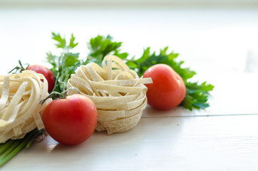 Tagliatelle with ingredients for cooking pasta. Curly parsley, garlic, tomatoes on a wooden table.