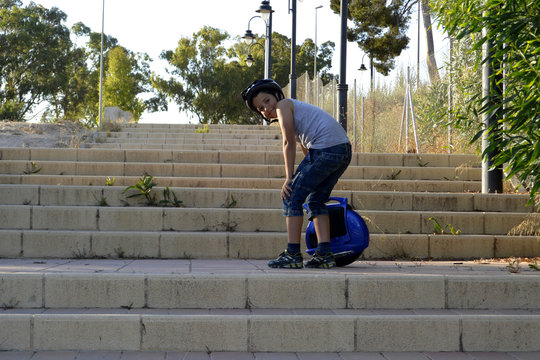 A boy with helmet is riding a Monowheel - mono scooter in the park