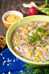 Okroshka. Traditional Russian summer cold soup with sausage, vegetables and kvass in bowl on wooden background.
