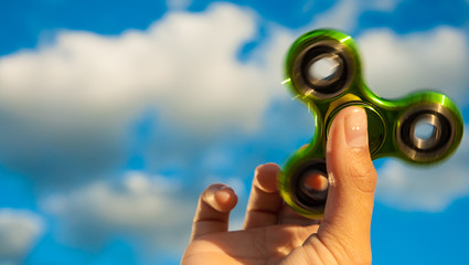 Hand holding popular green fidget spinner toy on sky background with copy space.