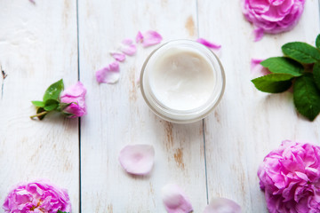 Natural cosmetic cream skincare product wellness and relaxation surrounded by rose blossom on white wooden table