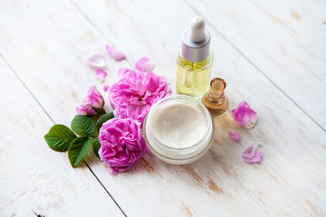 Spa setting with pot of moisturizing cream beautiful pink roses and rose oil on white background