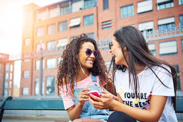 Girlfriends sitting outside listening to music on earphones