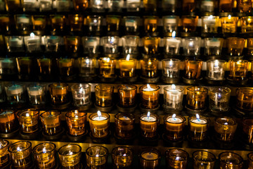 Macro closeup of many yellow candles with flame in church - obrazy, fototapety, plakaty