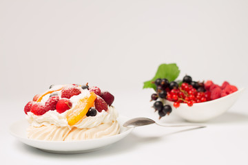 Meringue cake with strawberries, raspberry, peach, black currant, cherry and cream. A porcelain saucer with fresh fruits  in the background