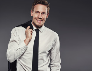 Stylish young businessman smiling and standing against a grey background