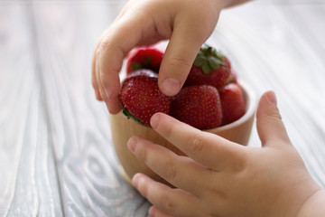 child's hands hold a bowl with strawberries