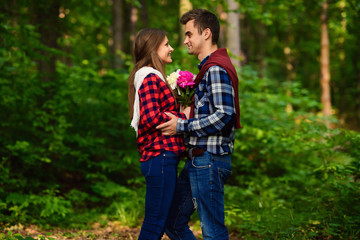 Fototapeta premium Stylish young couple in shirts and jeans while walking in the forest. A charming girl and her handsome boyfriend are looking at each other.