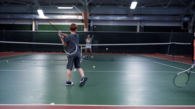 Team of two boys playing tennis against one more older girl or tennis coach